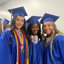 Three graduates pose for picture in blue graduation gowns